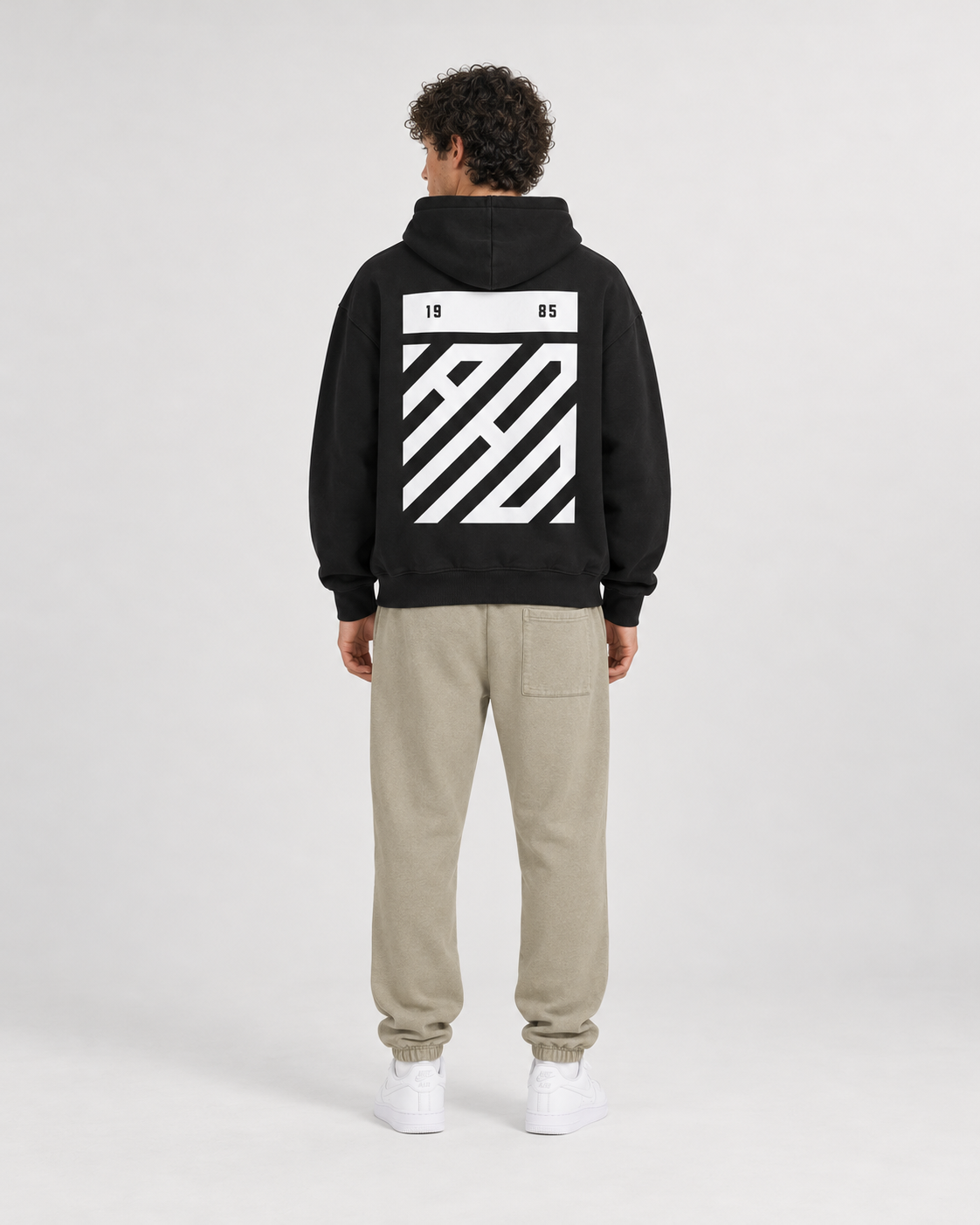 AI-generated styling illustration: AAO Tribute black hoodie with AAO Sandune sweatpants, back view.
